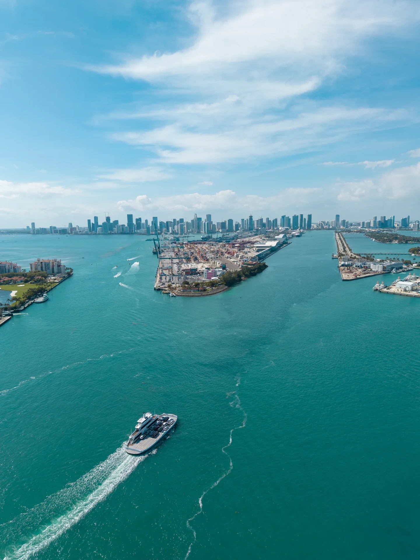 Aerial drone photo of a luxury yacht cruising Government Cut past PortMiami with the downtown Miami skyline beyond